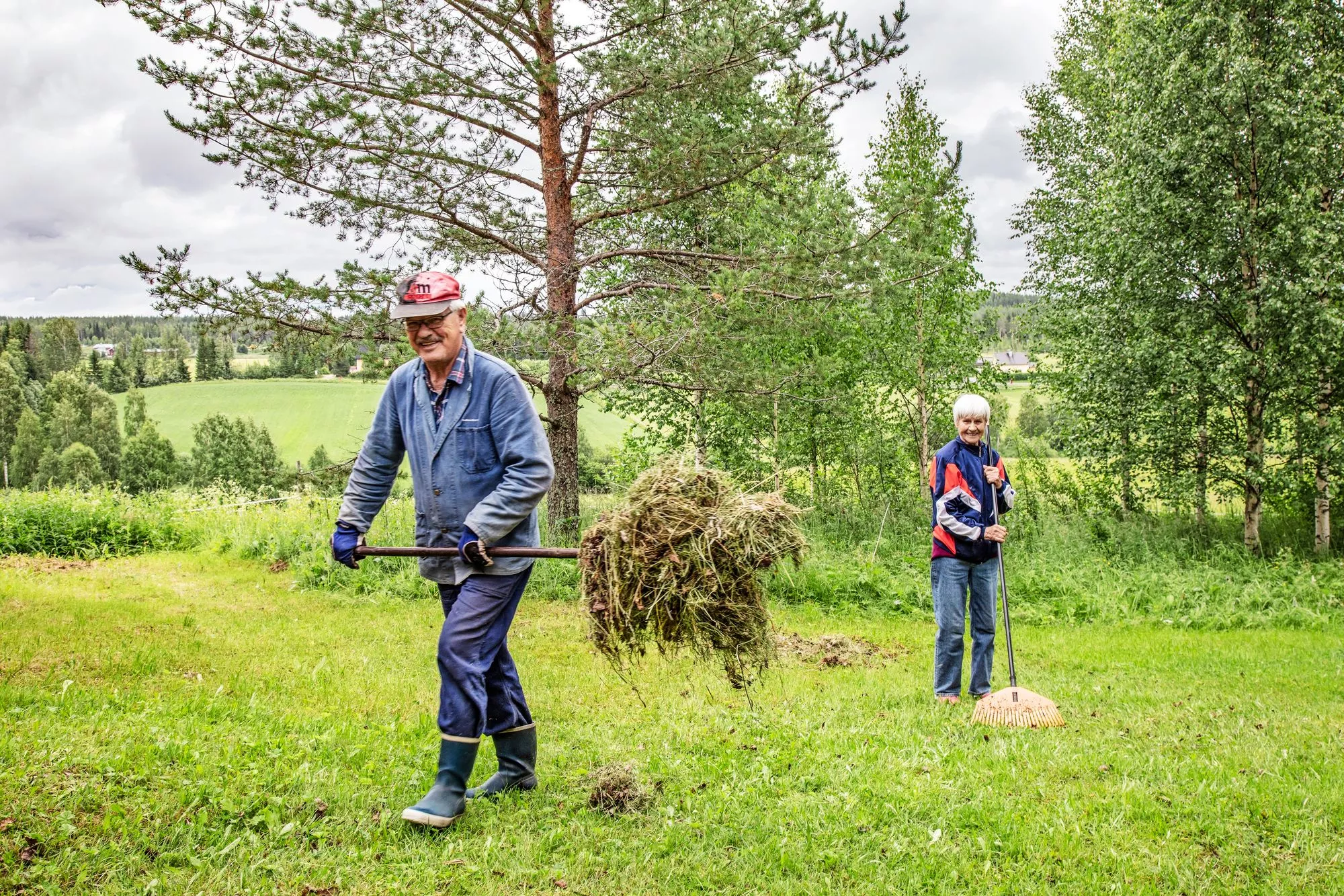 Reijo Säppi ja hänen isosiskonsa Sylvi Rautio haravoivat kotipihaa. Sisarukset palaavat tänne joka kesä. © Harri Mäenpää