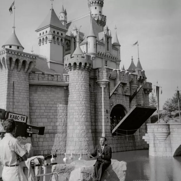 Walt Disney poseeraa Prinsessa Ruususen linnan edessä Disneylandin avajaispäivänä heinäkuussa 1955. Huvipuiston avajaiset televisioitiin ympäri Yhdysvaltoja.