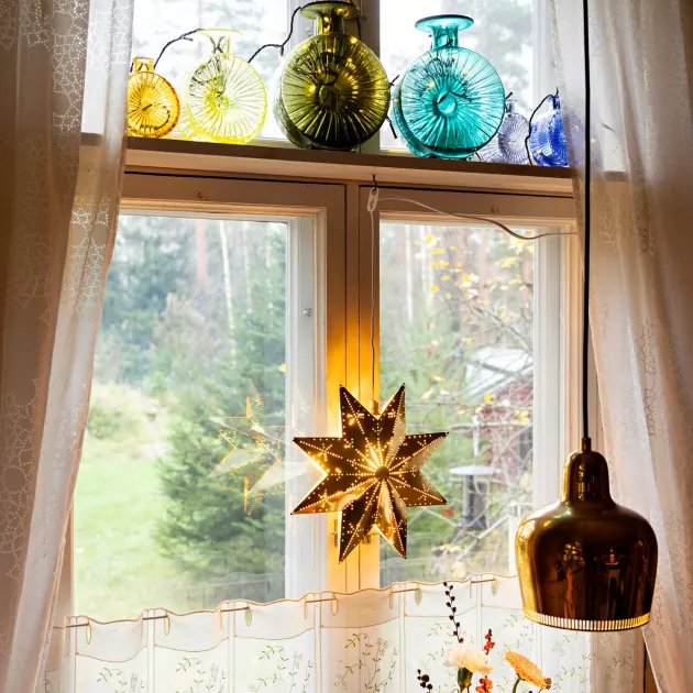 Keittiön ikkunasta avautuu näkymä metsään. Helena Tynellin suunnittelemat Aurinkopullotkin on koristeltu jouluvaloin.