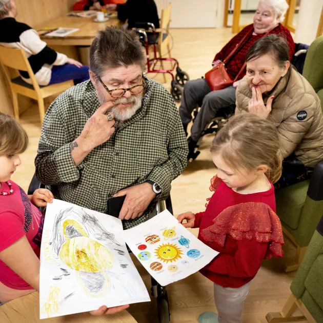 Sukupolvet kohtaavat. Eskarilaiset Jasmine (vas.) ja Isla näyttävät Ralf Öhmanille piirroksia ja kuvia planeetoista. Taustalla Raija Sumiloff ja Sirpa Koivikko.