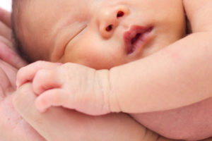 Kuvituskuva: vauva nukkuu aikuisen käsien päällä.