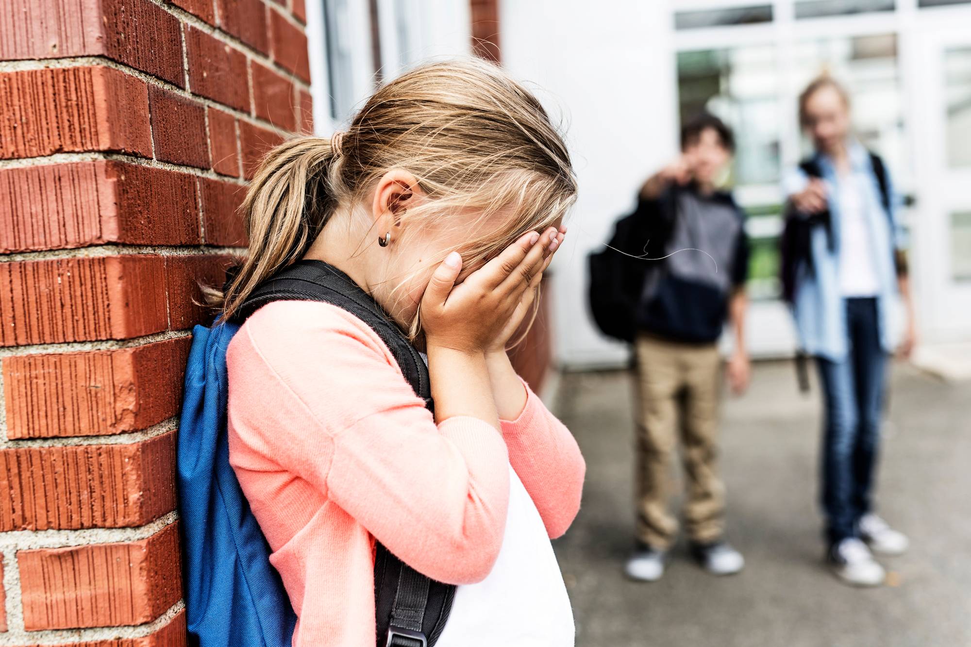Kuvituskuva: Tyttö itkee koulun kulmalla.