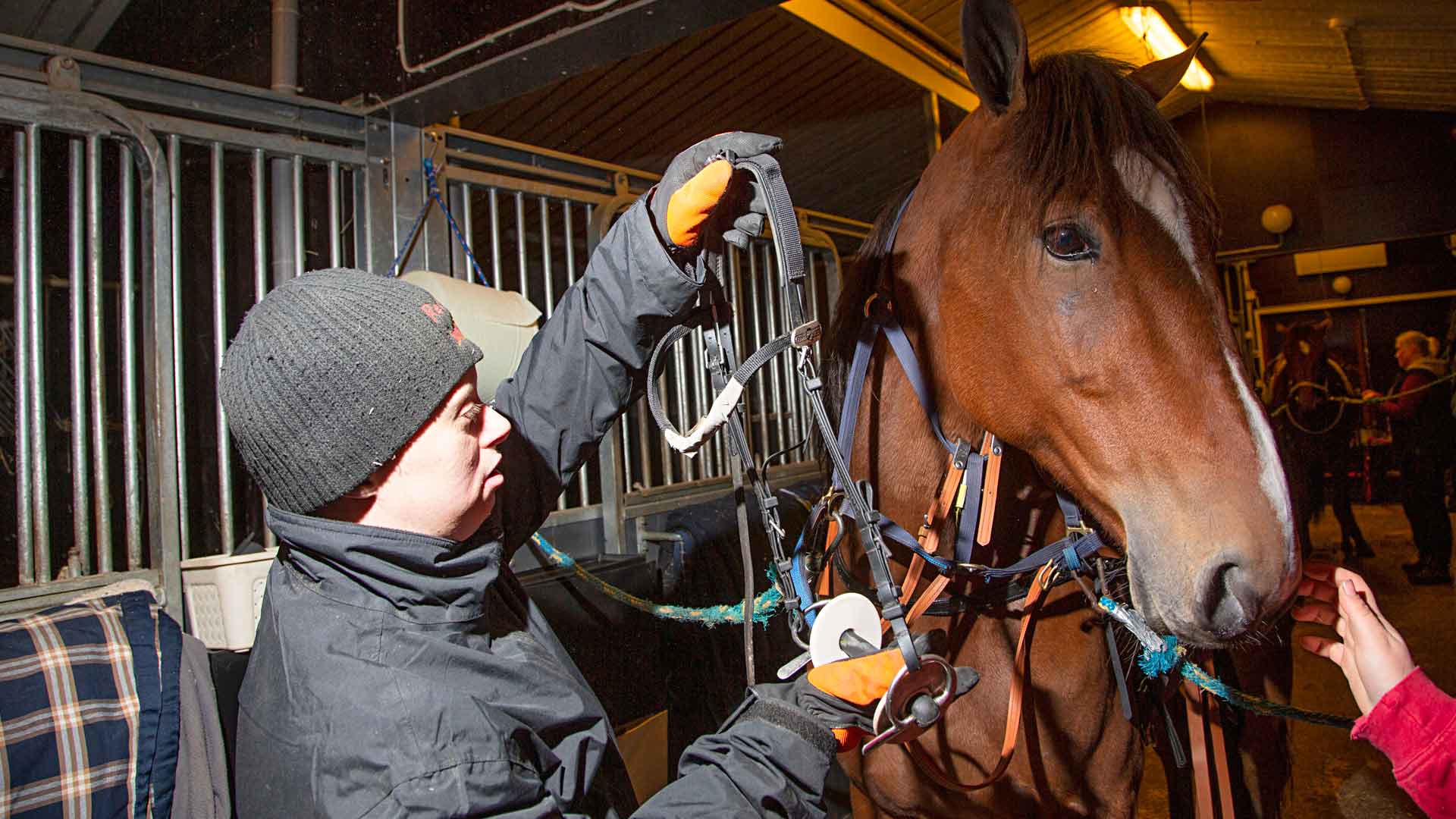 Päivätoiminnan asiakkaat auttavat tallitöissä ja hoitavat hevosia hevosammattilaisten ohjeiden mukaan. Miska lämmittää treeniin menevän hevosen kuolaimia. 