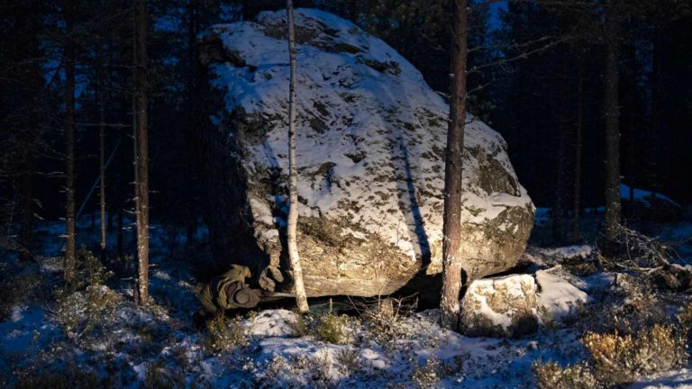 Muinaisuuden jälkiä kotiseutunsa metsistä etsivä Anssi Toivanen kurkistelee Leppävirran Tilkonvuoren Jättiläisenkiven alle.