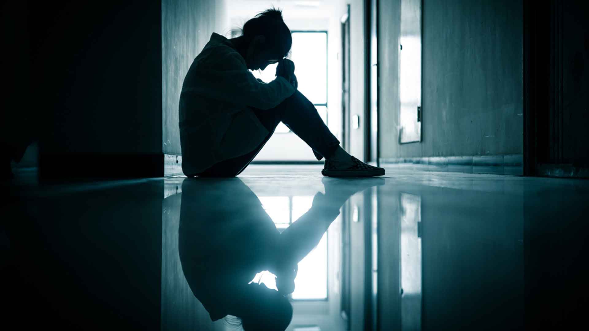 Surullinen tyttö istuu pimeällä käytävällä. Koululääkärit eivät ehdi auttaa kaikkia.