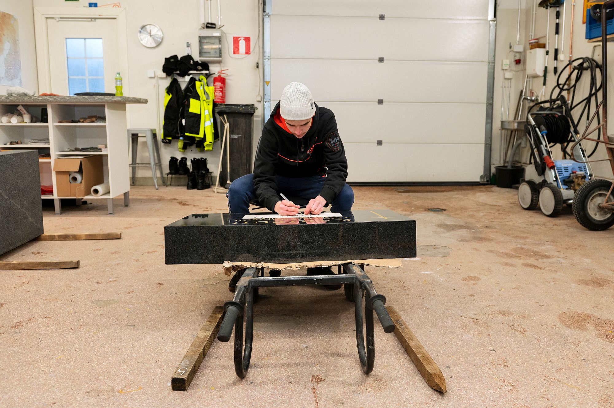 Hautakiviä tehdessä on tärkeää huolehtia hyvästä työasennosta. Kasper Kokko on sisällä lämpimässä hallissa, isoisä oli aikoinaan polvillaan laudoilla haudan päällä. © Linda Varoma