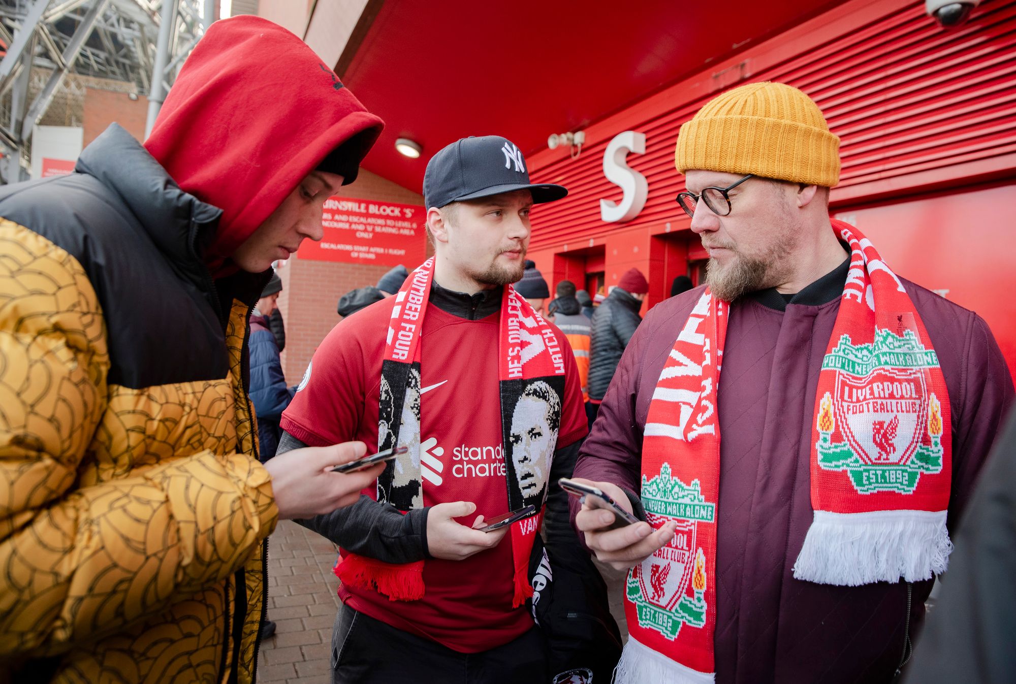 Emil (vas.), Timi ja Markku Ketola valmistautuvat matkansa huipennukseen ja ottavat puhelimista esille pääsyliput FC Liverpoolin kotiotteluun.  © Aku Ratsula